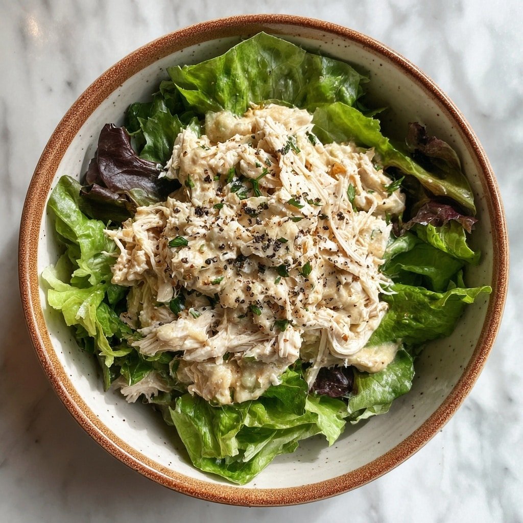 A round bowl with a speckled brown rim holds a fresh salad. The bottom layer is bright green lettuce leaves around the edges. On top, there is a creamy light beige mixture with small chunks and a soft texture. The top layer shows white shredded chicken pieces sprinkled with black pepper. The bowl sits on a white marbled surface. photo taken with an iphone --ar 1:1 --v 7 — Crockpot Chicken Caesar Salad, slow cooker Caesar salad, easy healthy chicken salad, casual dinner recipes, make-ahead chicken salads